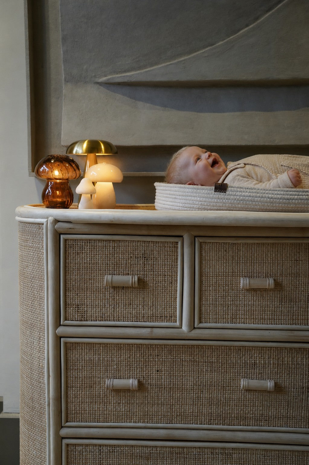 Naturel rotan commode met aankleedkussen en baby in een warme, stijlvolle babykamer