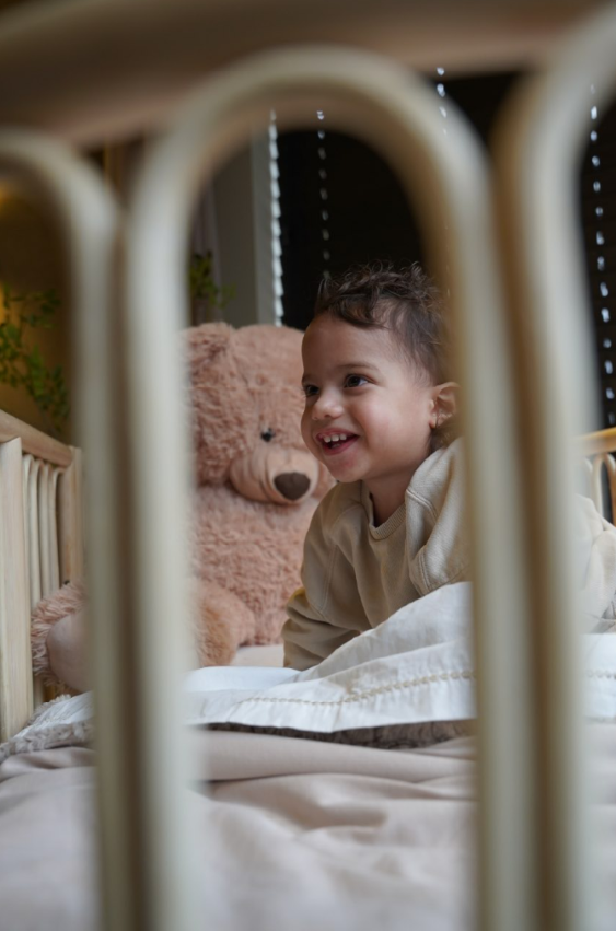 Blije peuter speelt in een rotan meegroeibed met afgeronde spijlen en veilige, geborgen slaapomgeving