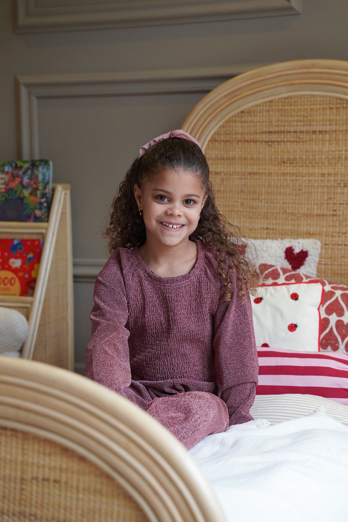 Kind in een naturel rotan kinderbed met afgerond hoofdbord in een warme, sfeervolle kinderkamer