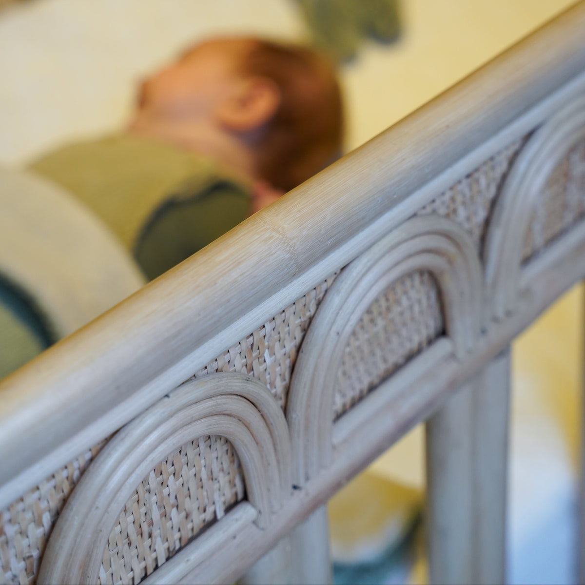 Detail van een naturel rotan babybed met handgevlochten afwerking en slapende baby