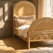 Naturel rotan kinderbed met handgevlochten hoofdbord en afgeronde afwerking in een warme kinderkamer