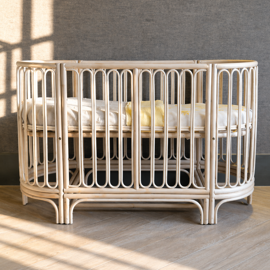Vooraanzicht van het 4-in-1 Cosy meegroeibed in babybed-opstelling, vervaardigd uit natuurlijk rotan met handgevlochten panelen, afgeronde spijlen, een in hoogte verstelbare bedbodem en een tijdloos boho design dat meegroeit van babybed naar peuter- en juniorbed.