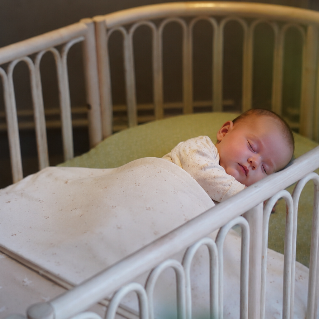 Slapende baby in een veilig rotan babybed met afgeronde spijlen en comfortabele matras