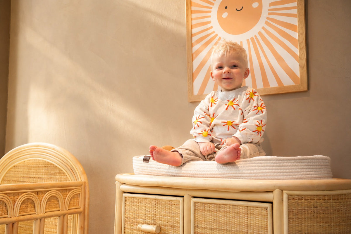 Blije baby in een veilig rotan babybed met afgeronde spijlen en comfortabele matras