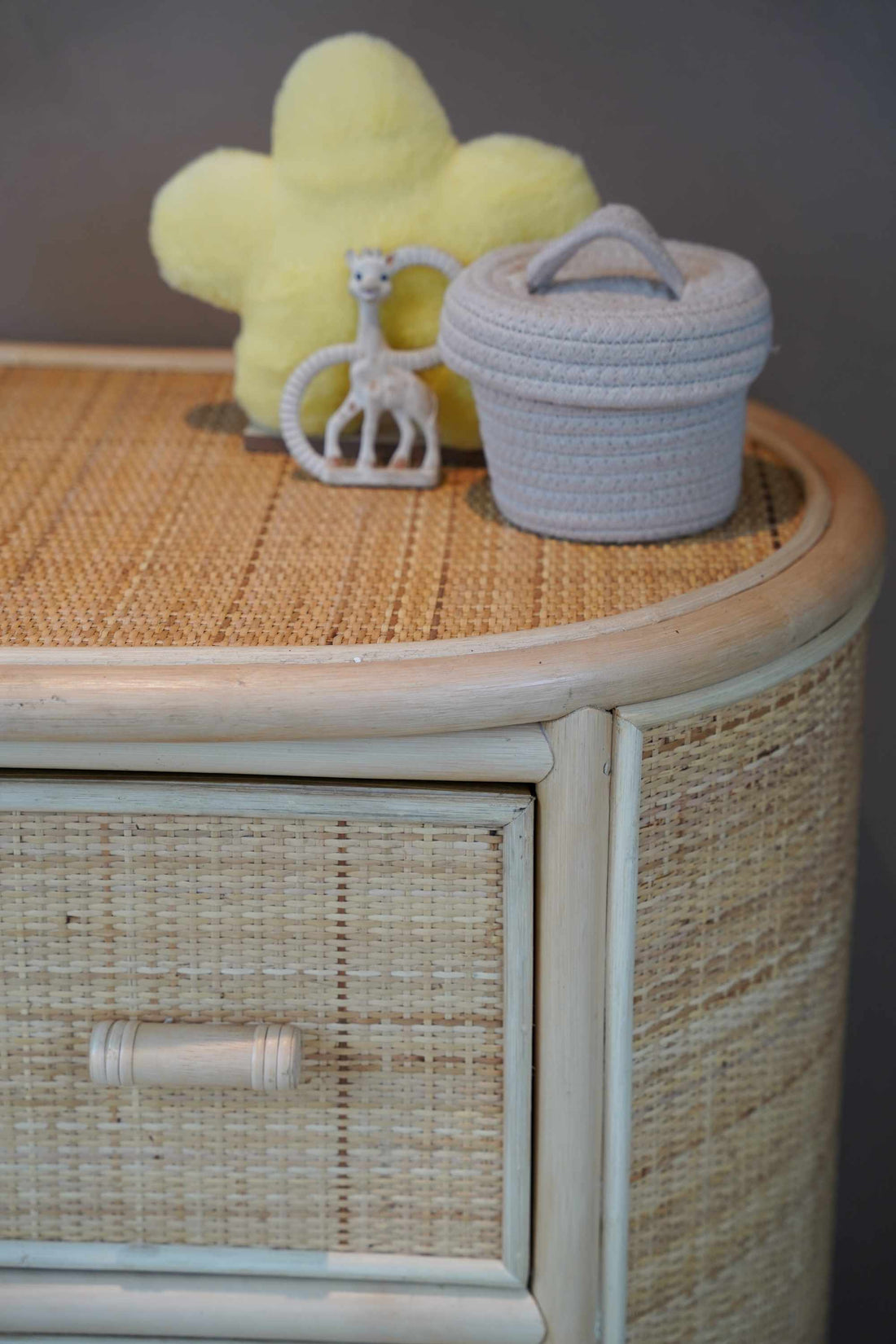 Close-up van de Sunny Home Store commode van natuurlijk rotan met handgevlochten afwerking, afgeronde hoeken en houten handgreep, gestyled met zachte babydecoratie op het ruime bovenblad voor een warme en natuurlijke babykamer.
