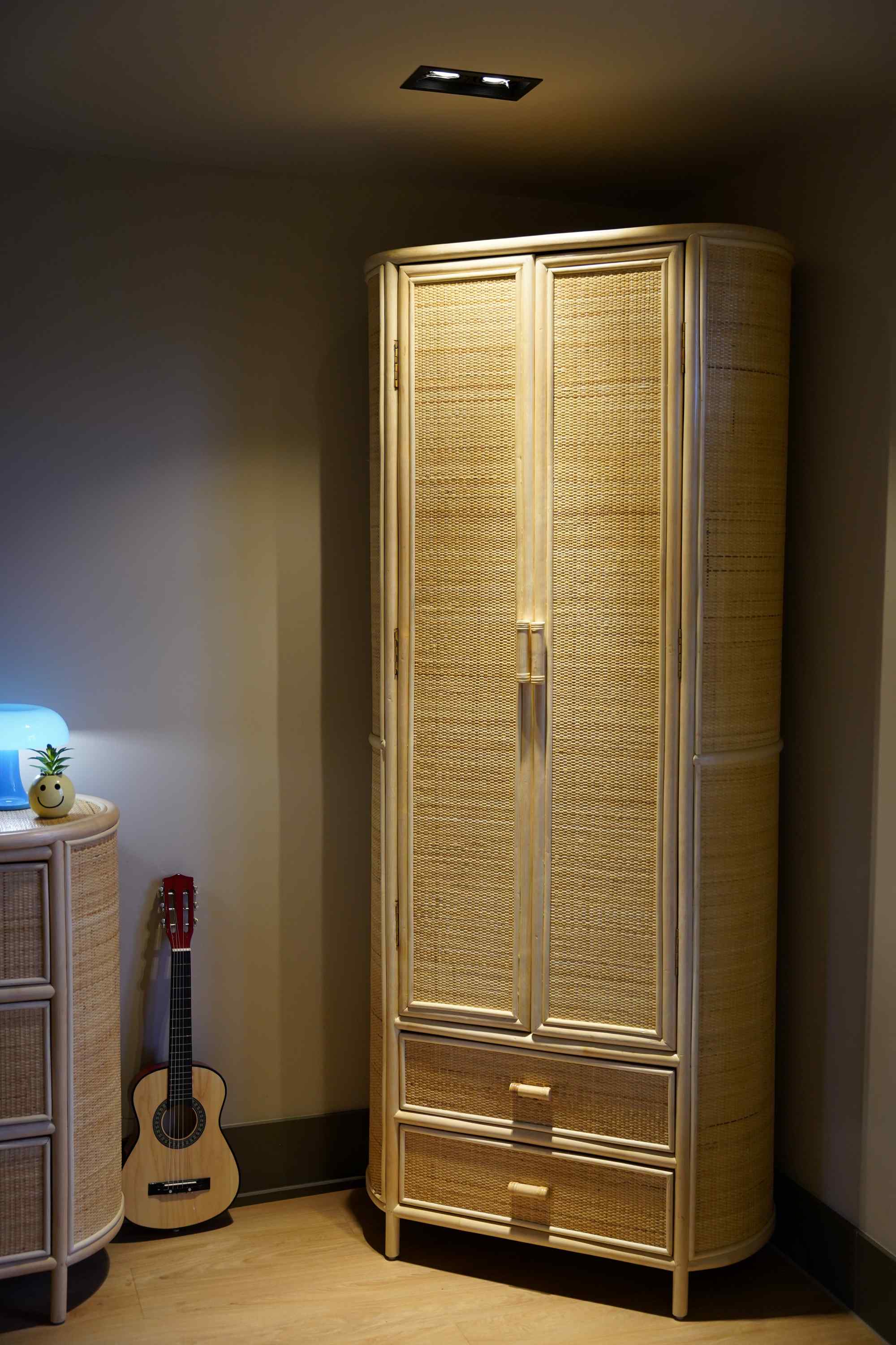 Rotan kledingkast uitgelicht met een spot in een babykamer interieur met beige tinten.
