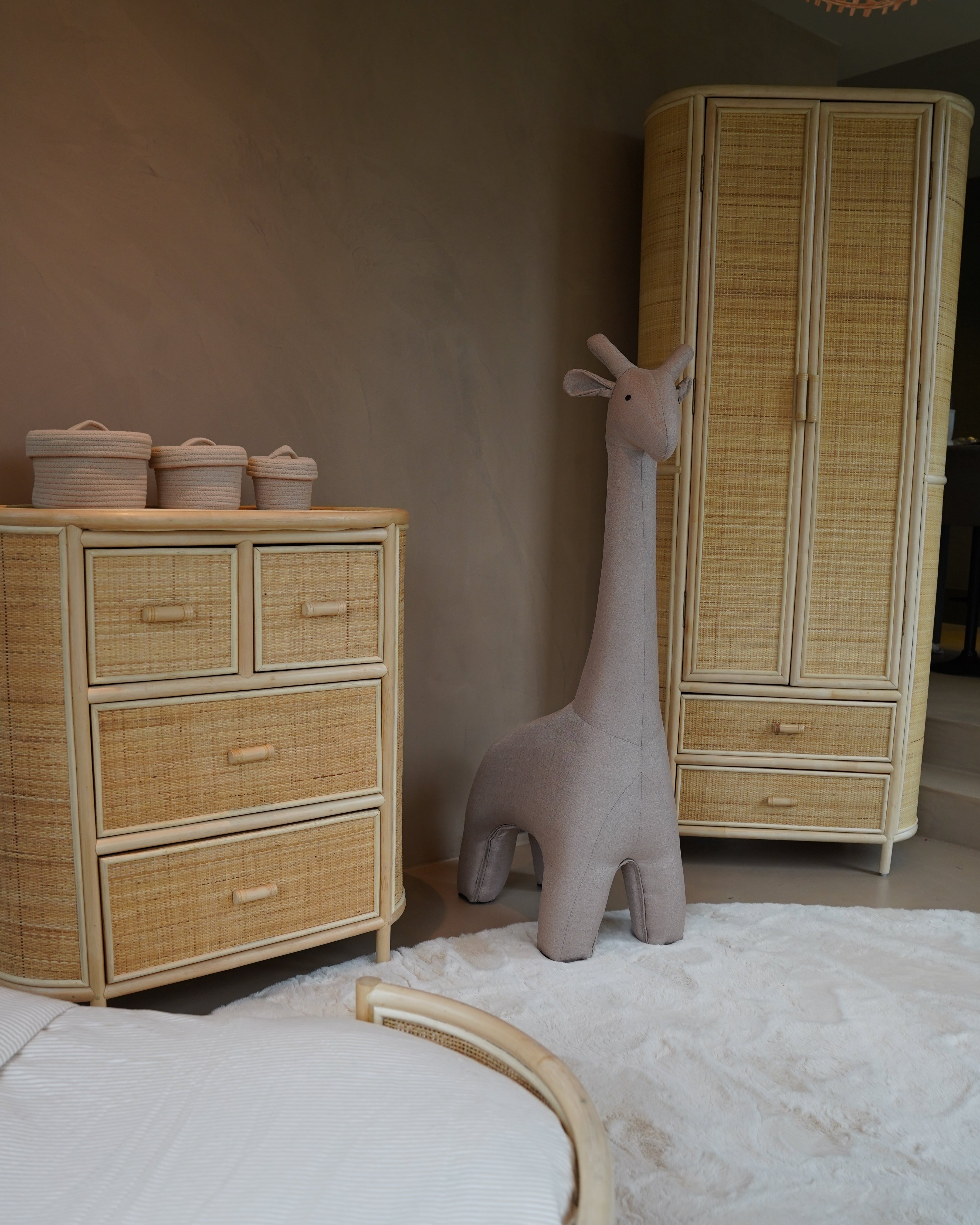 Rotan kledingkast en commode in een babykamer interieur met witte en beige tinten.
