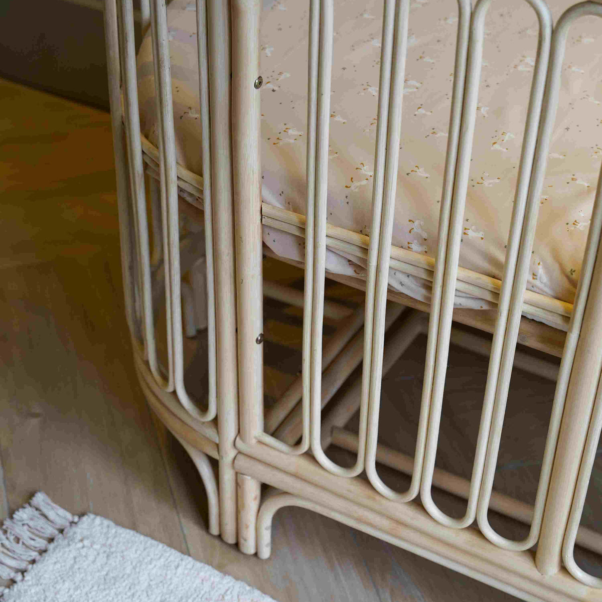 Detailfoto van het 4-in-1 Cosy meegroeibed met afgeronde rotan spijlen, handgevlochten afwerking en verstelbare bedbodem, ontworpen voor een veilige, duurzame en stijlvolle babykamer.
