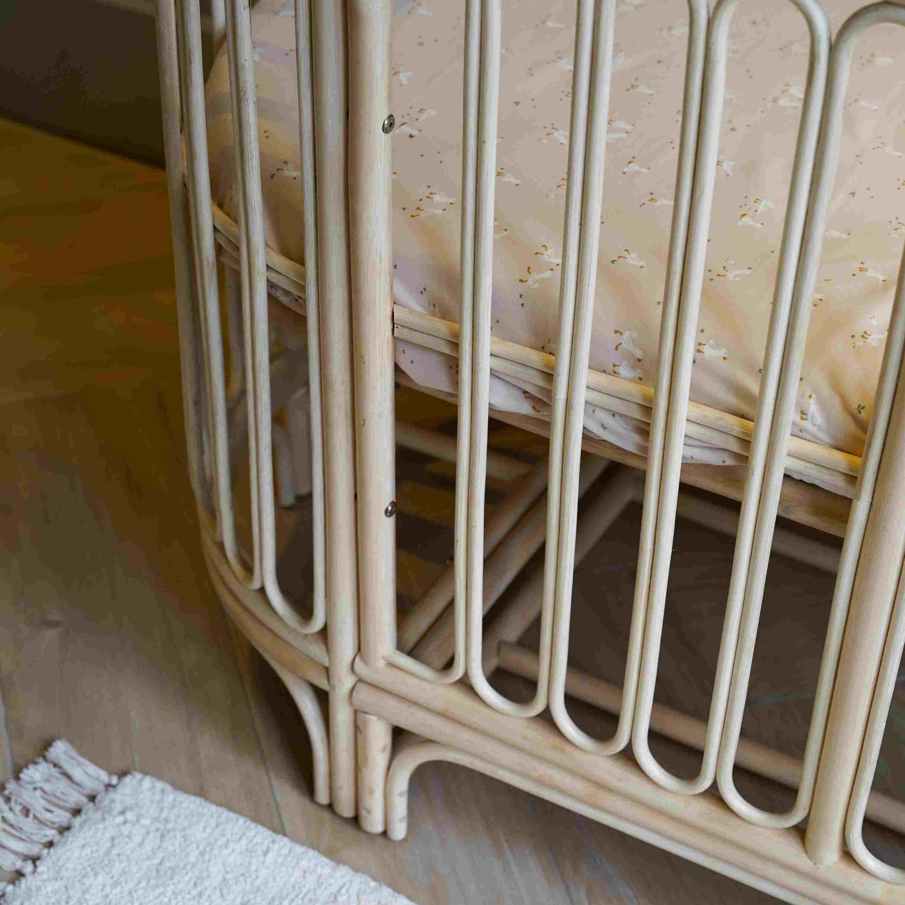 Detailfoto van het 4-in-1 Cosy meegroeibed met afgeronde rotan spijlen, handgevlochten afwerking en verstelbare bedbodem, ontworpen voor een veilige, duurzame en stijlvolle babykamer.