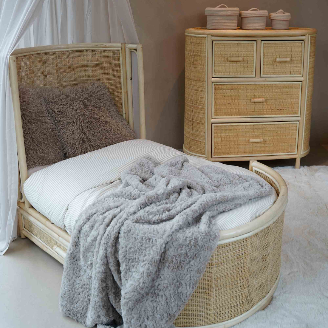 Sfeervolle lifestylefoto van het Rainbow juniorbed en de bijpassende Sunny Home Store commode van natuurlijk rotan. Het handgemaakte meubelset met handgevlochten rotan details, afgeronde vormen en ruime opberglades creëert een warme, rustgevende en tijdloze kinderkamer in natuurlijke boho stijl.