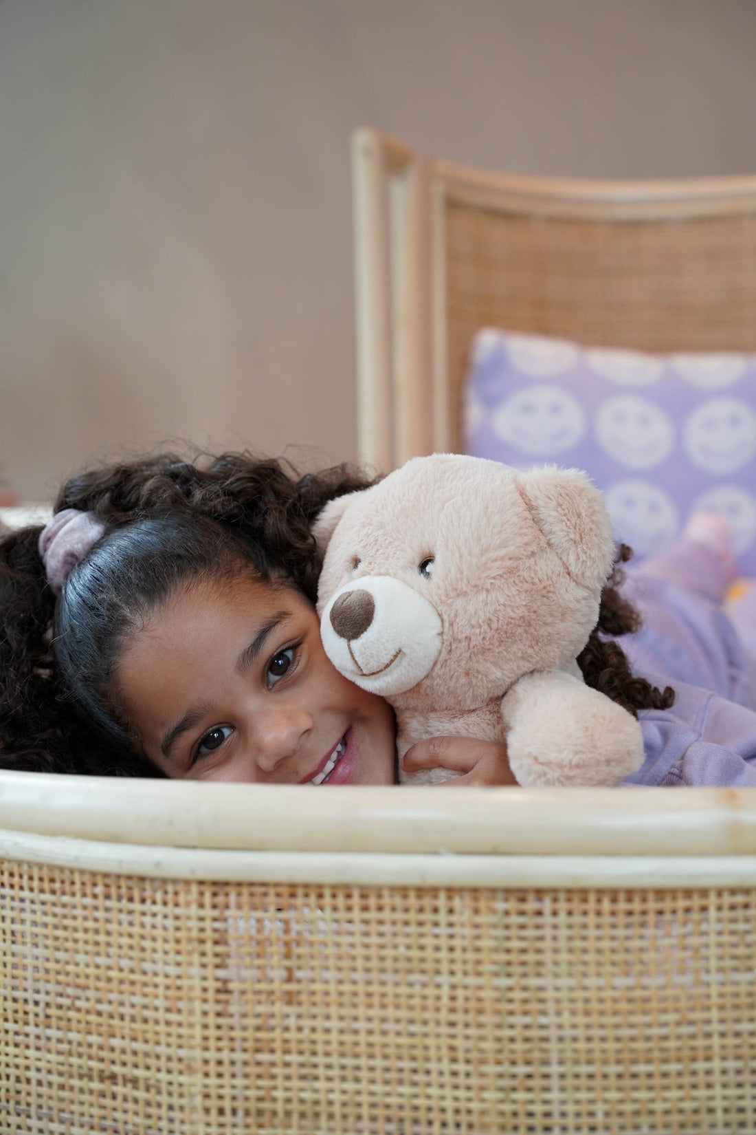 Sfeervolle lifestylefoto van het Rainbow juniorbed van natuurlijk rotan, waarop een kind ontspannen zit. Het handgevlochten hoofdbord en de warme boho uitstraling maken het bed een stijlvolle keuze voor de kinderkamer vanaf circa 5 jaar.