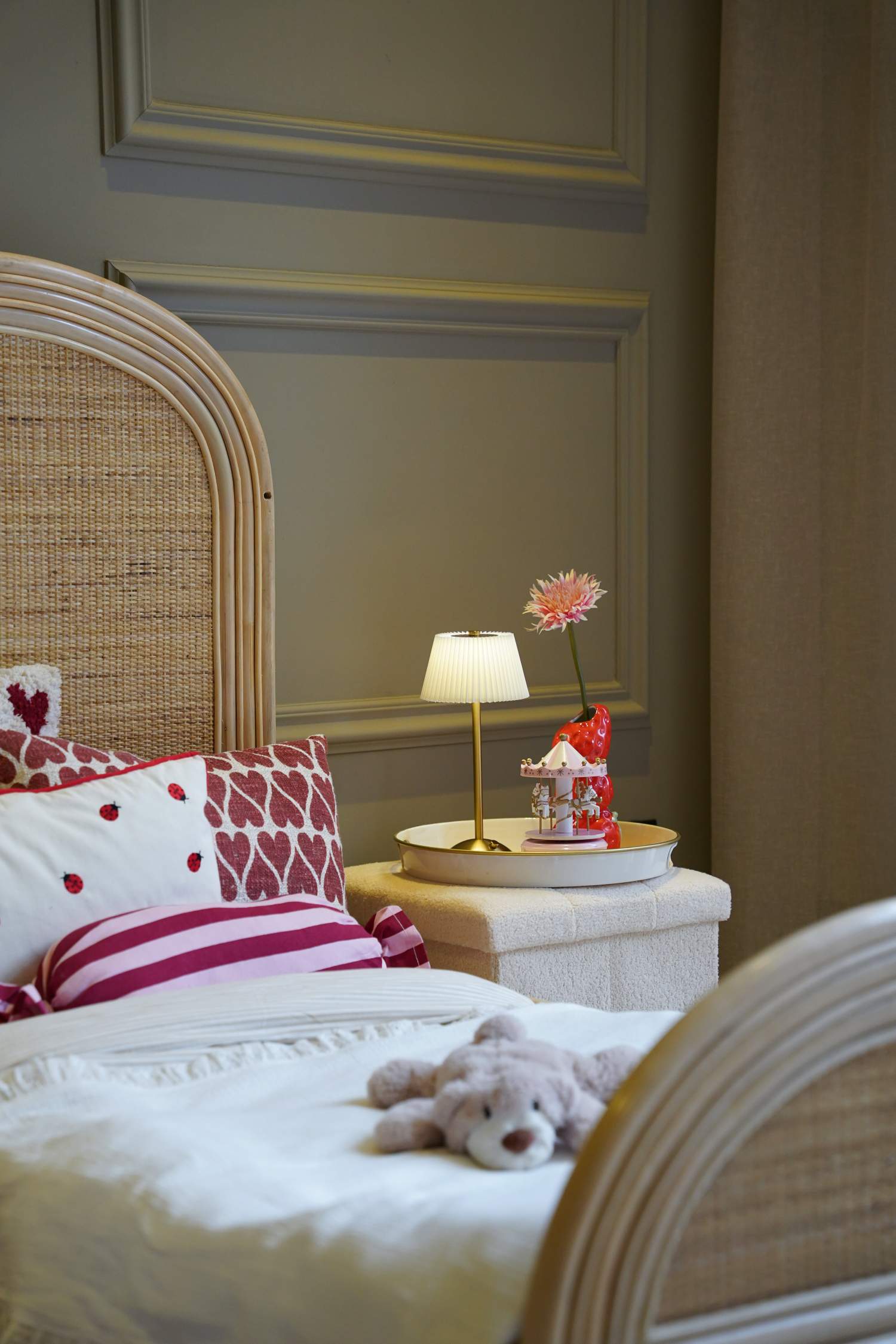 Sfeervolle lifestylefoto van het Rainbow juniorbed van natuurlijk rotan met handgevlochten hoofdbord en afgeronde vormen. Het bed is gestyled met zacht beddengoed, kleurrijke sierkussens en een nachttafeltje met verlichting voor een warme, knusse en stijlvolle kinderkamer.